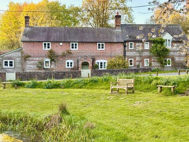 The 18th‑century brick and flint cottage in Tollard Royal, seen across the village green in spring